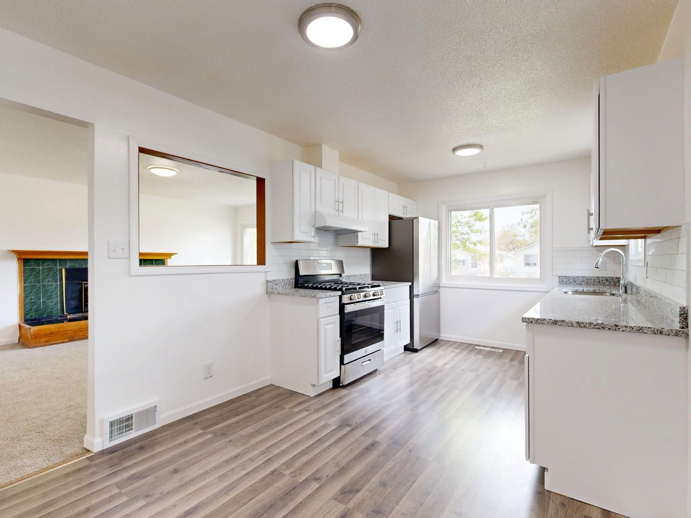 Bright renovated kitchen with white cabinets, granite counters, and wood-look flooring