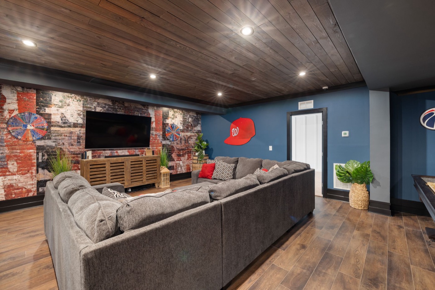 Finished basement family room with wood-plank ceiling, sectional sofa, and wall-mounted TV