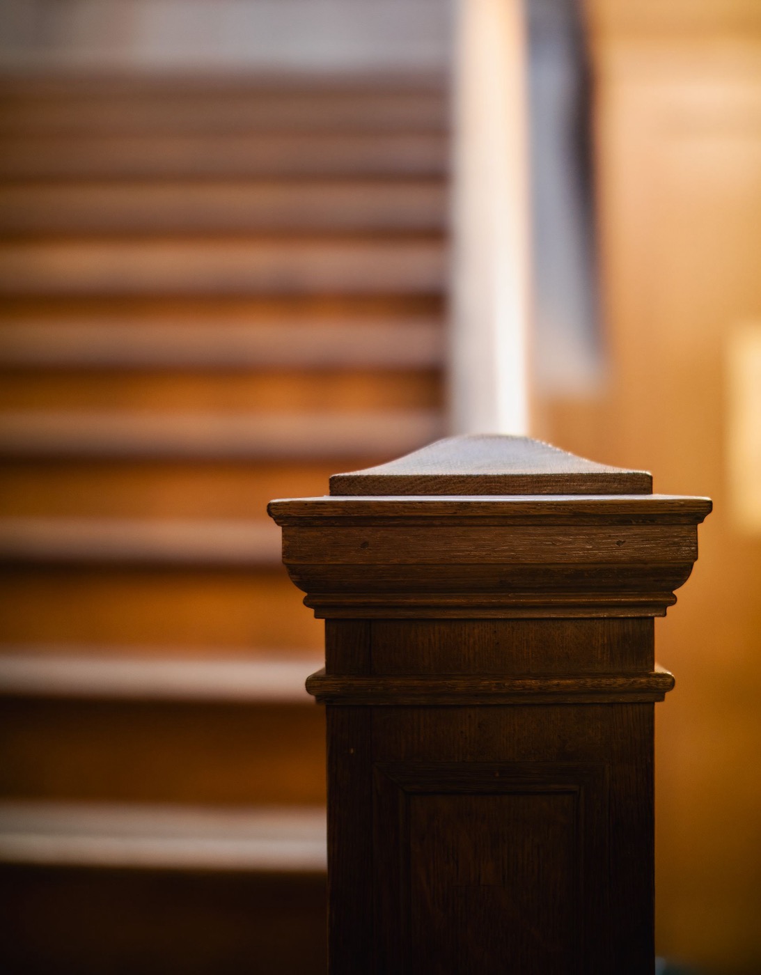 Close-up of a dark wood stair newel post detail in warm interior light